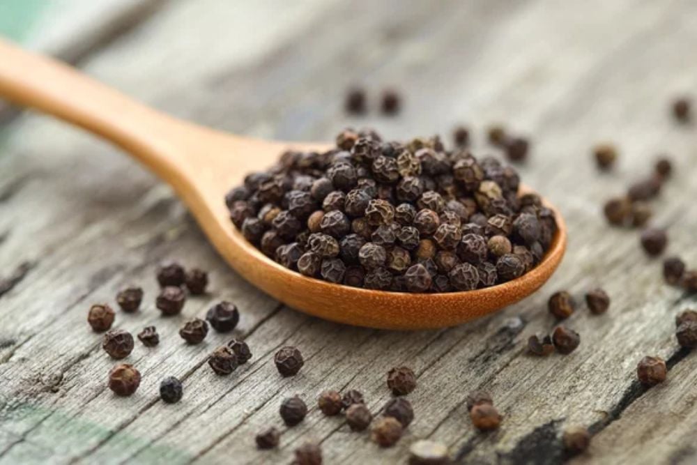 Whole black pepper on wooden spoon — Stock Photo, Image